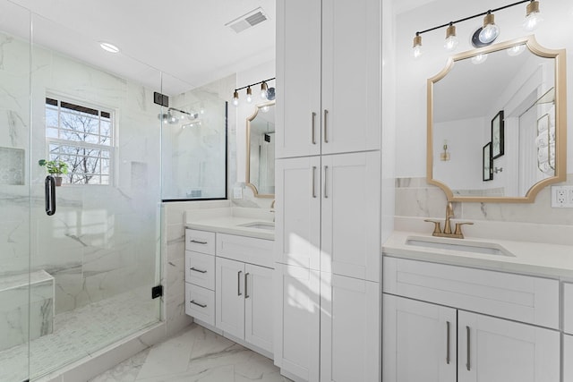 bathroom with a marble finish shower, visible vents, two vanities, marble finish floor, and a sink