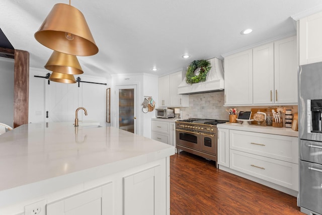 kitchen featuring light countertops, a barn door, appliances with stainless steel finishes, custom exhaust hood, and a sink