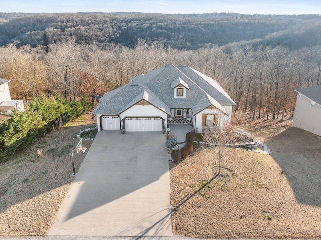 view of front of house featuring a garage, a forest view, driveway, and a shingled roof