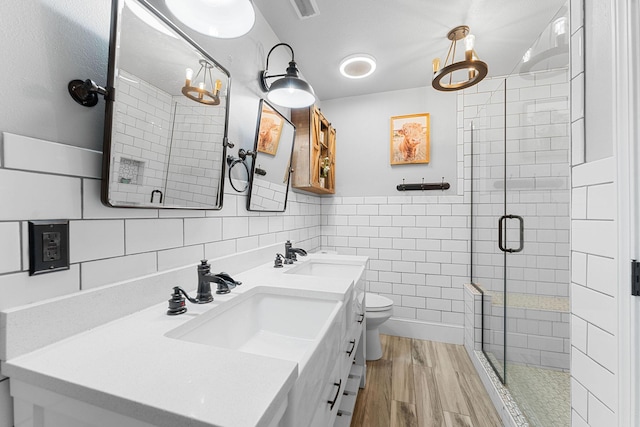 bathroom with wood finished floors, a stall shower, a sink, tile walls, and toilet