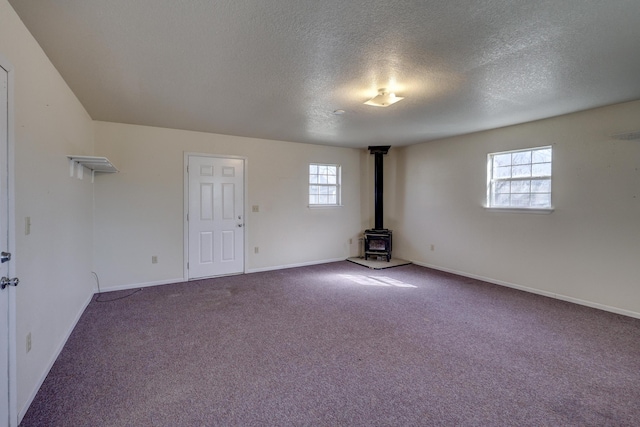 carpeted empty room featuring a textured ceiling, a wood stove, and baseboards