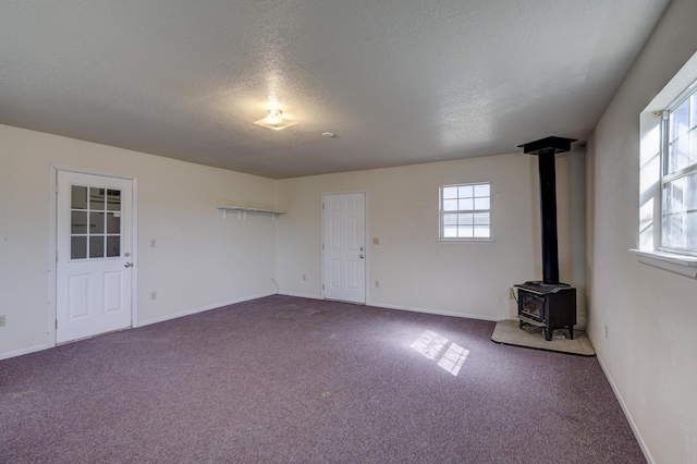 carpeted spare room with a wealth of natural light, a textured ceiling, a wood stove, and baseboards