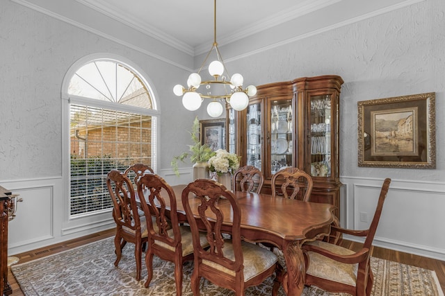 dining room with crown molding, wood finished floors, wainscoting, an inviting chandelier, and a textured wall