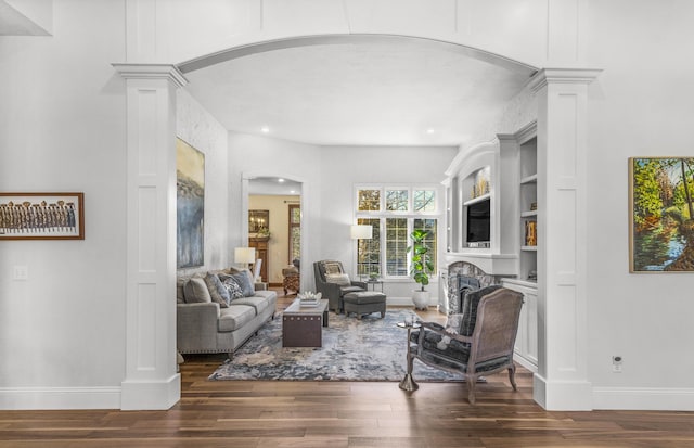 living area featuring a fireplace, wood finished floors, baseboards, and ornate columns