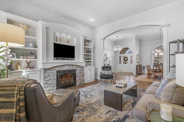 living room with built in shelves, wood finished floors, arched walkways, a stone fireplace, and an inviting chandelier