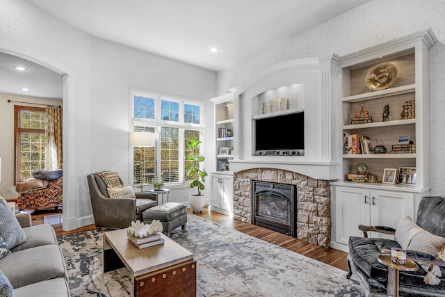 living area with built in features, a healthy amount of sunlight, a fireplace, and wood finished floors