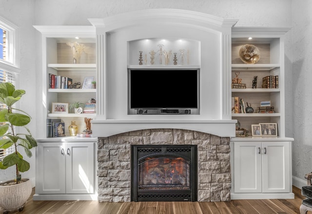 living room with built in shelves, a stone fireplace, wood finished floors, and a textured wall