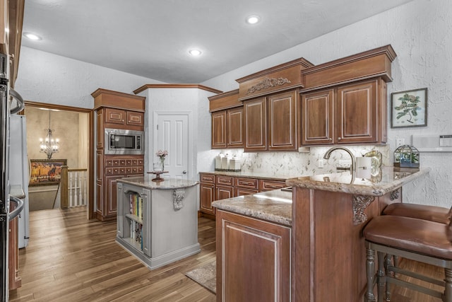 kitchen featuring light stone counters, wood finished floors, a peninsula, stainless steel microwave, and a textured wall