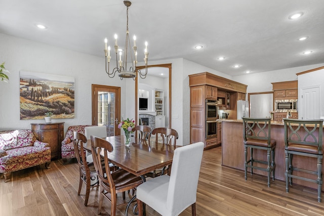 dining area featuring recessed lighting, a fireplace, an inviting chandelier, and wood finished floors