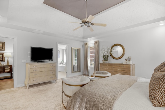 bedroom with light colored carpet, a tray ceiling, vaulted ceiling, ensuite bath, and a ceiling fan