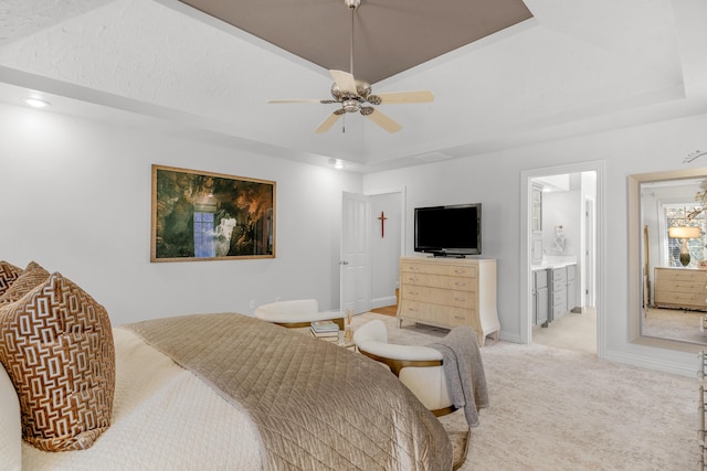 bedroom with baseboards, light carpet, ensuite bathroom, a raised ceiling, and a ceiling fan