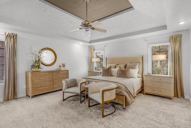 bedroom with baseboards, light colored carpet, a textured ceiling, and a tray ceiling