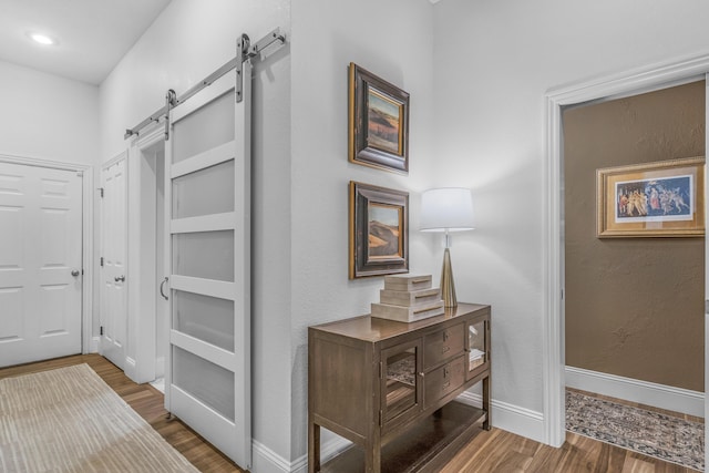 hallway featuring a barn door, wood finished floors, and baseboards