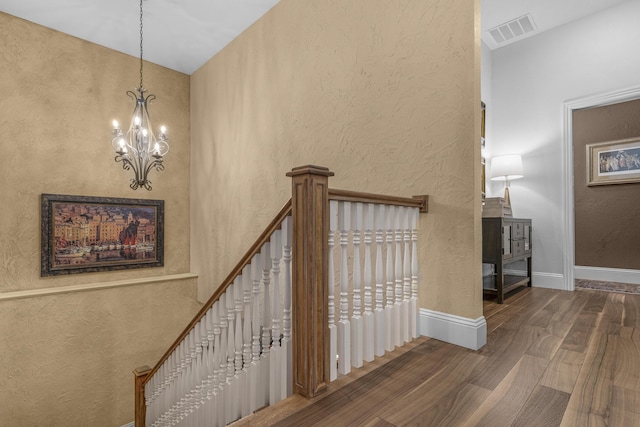 staircase with visible vents, wood finished floors, an inviting chandelier, baseboards, and a textured wall