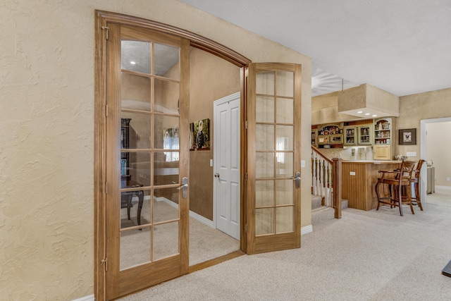 corridor featuring french doors, baseboards, carpet, and a textured wall