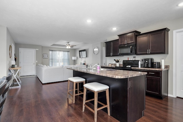 kitchen featuring a breakfast bar, dark wood-style flooring, black appliances, dark brown cabinetry, and open floor plan