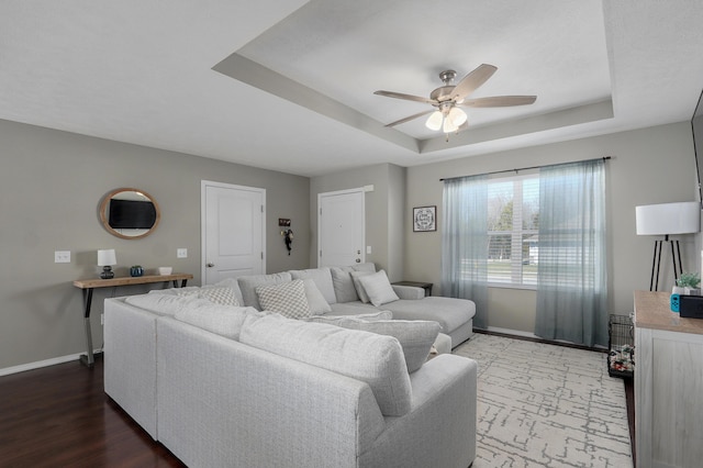 living area featuring ceiling fan, a raised ceiling, baseboards, and wood finished floors