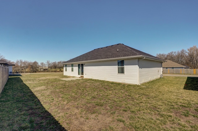 rear view of house featuring a lawn, a shingled roof, and fence