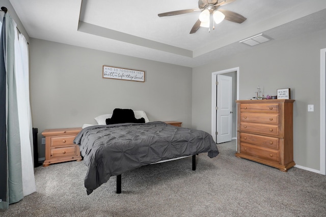 carpeted bedroom with a tray ceiling, visible vents, baseboards, and ceiling fan