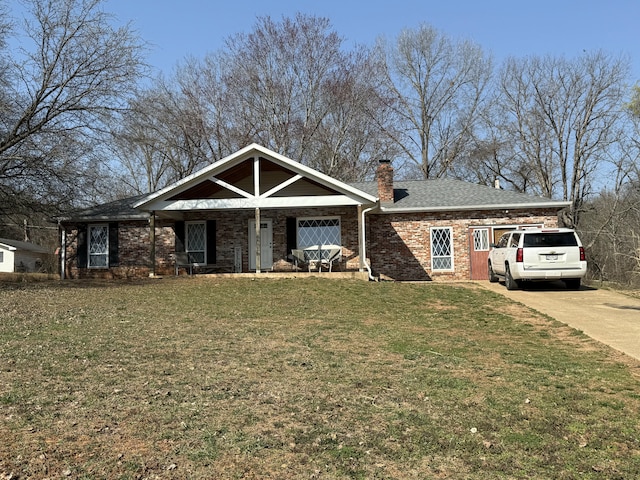 view of front facade with roof with shingles, concrete driveway, a front yard, brick siding, and a chimney