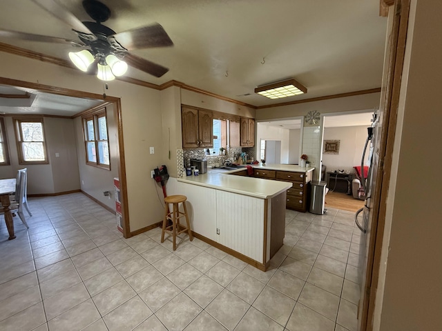 kitchen with a peninsula, a sink, decorative backsplash, ceiling fan, and crown molding