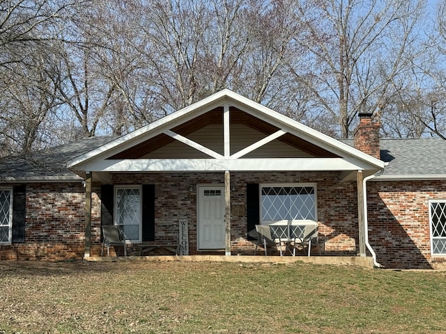 view of front of property with a front lawn, a porch, a shingled roof, brick siding, and a chimney