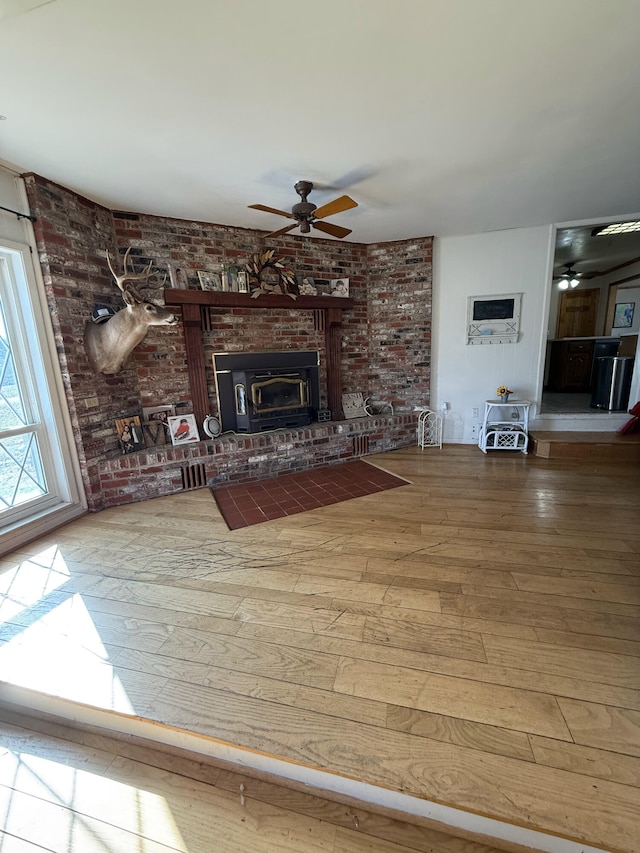 unfurnished living room featuring hardwood / wood-style floors, a brick fireplace, a ceiling fan, and brick wall