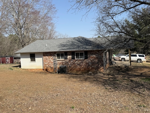 exterior space with an outbuilding, brick siding, central AC, and a shingled roof