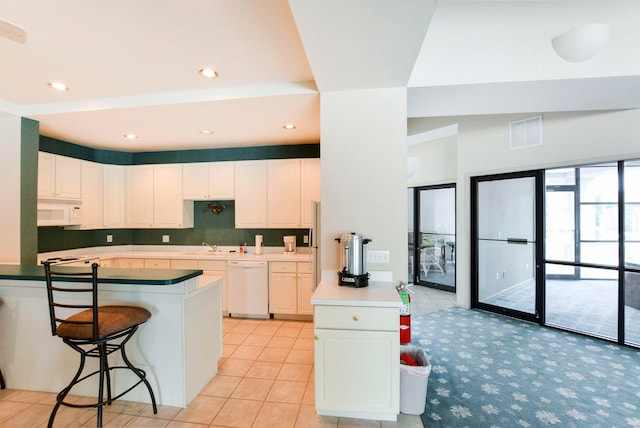 kitchen with white appliances, a breakfast bar area, visible vents, a peninsula, and white cabinets