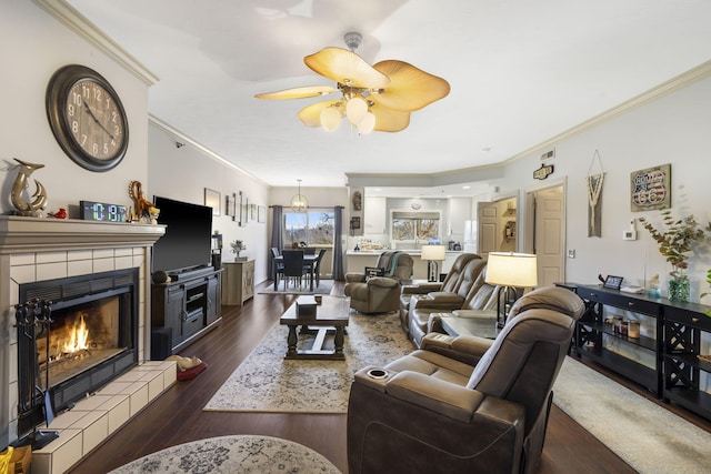 living area with a tiled fireplace, crown molding, dark wood finished floors, and a ceiling fan