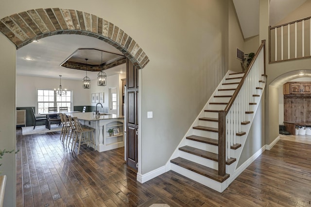 stairway featuring arched walkways, a chandelier, baseboards, and hardwood / wood-style flooring