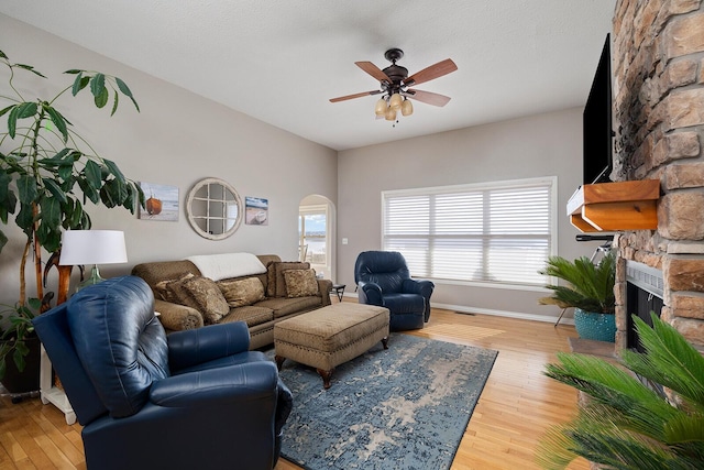 living room with light wood-type flooring, arched walkways, a fireplace, baseboards, and ceiling fan