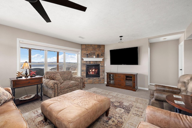 living area featuring ceiling fan, a fireplace, baseboards, and a textured ceiling