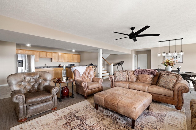 living area featuring stairway, light wood-style flooring, a textured ceiling, and a ceiling fan