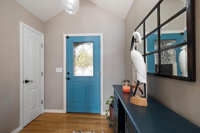 entryway with lofted ceiling, wood finished floors, baseboards, and a textured ceiling