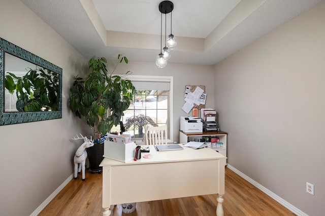 office featuring baseboards, a raised ceiling, and light wood finished floors