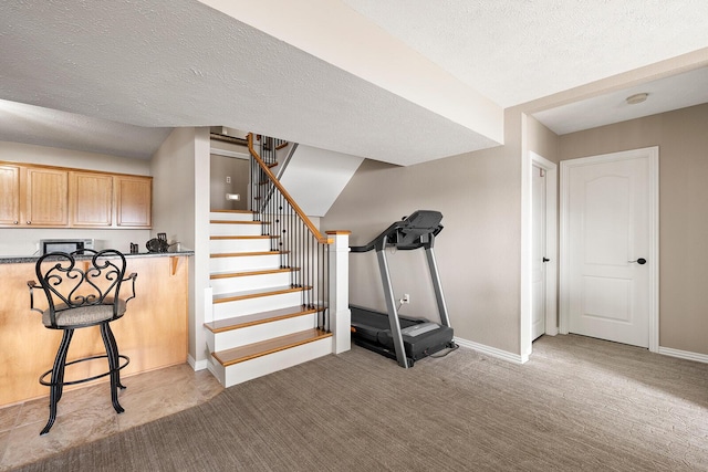 basement with light carpet, a textured ceiling, stairs, and baseboards