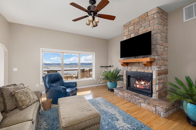 living room with visible vents, baseboards, a stone fireplace, wood finished floors, and arched walkways