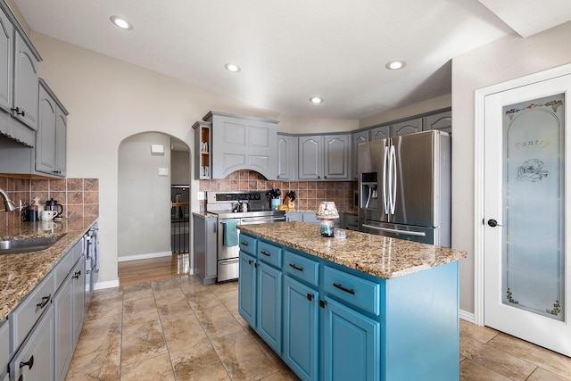 kitchen featuring a center island, light stone counters, arched walkways, stainless steel appliances, and a sink