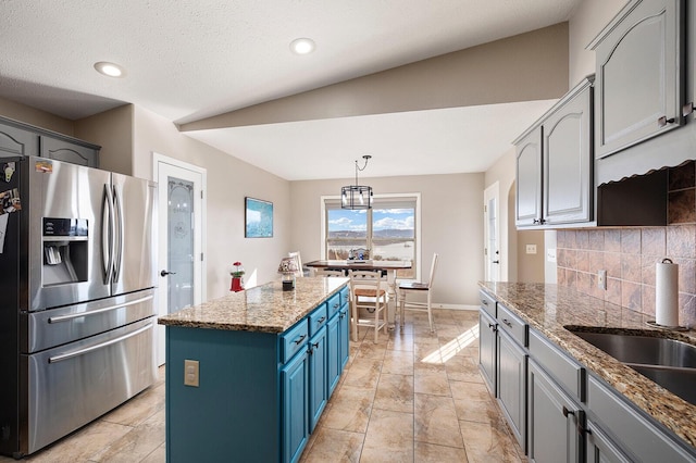 kitchen with stainless steel fridge with ice dispenser, stone countertops, blue cabinets, tasteful backsplash, and a center island