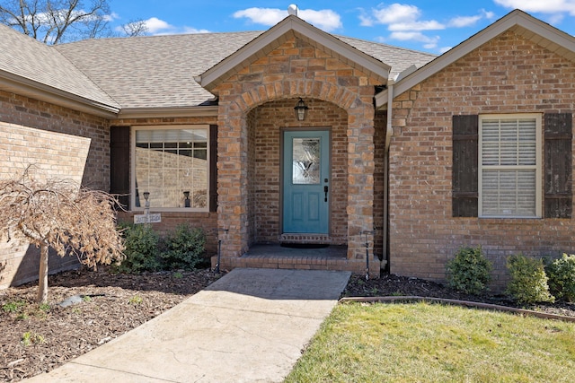 view of exterior entry with brick siding and roof with shingles