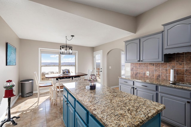 kitchen featuring arched walkways, tasteful backsplash, light stone countertops, and a kitchen island