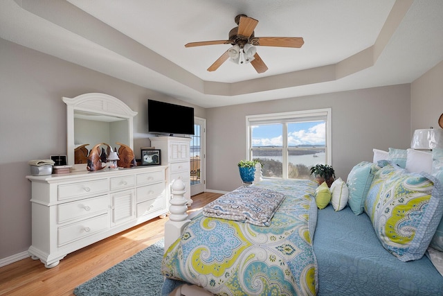 bedroom with a raised ceiling, baseboards, light wood-type flooring, and ceiling fan