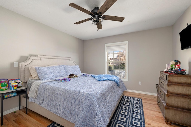 bedroom with light wood finished floors, a ceiling fan, and baseboards