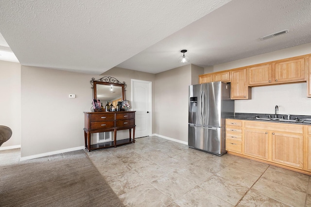 kitchen featuring dark countertops, visible vents, baseboards, stainless steel refrigerator with ice dispenser, and a sink