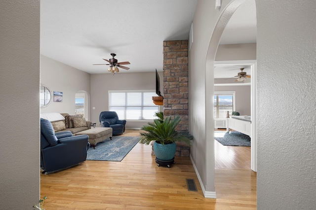 living room featuring arched walkways, visible vents, light wood-type flooring, and a ceiling fan