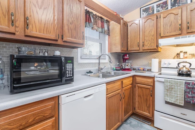 kitchen with under cabinet range hood, light countertops, white appliances, a textured ceiling, and a sink