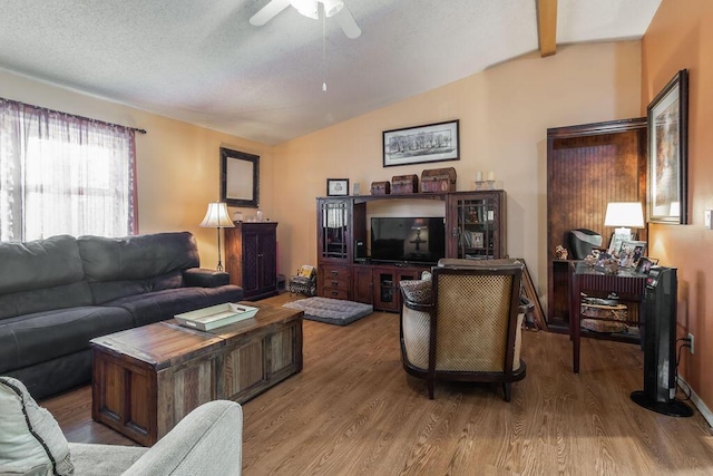 living area with lofted ceiling with beams, a textured ceiling, wood finished floors, and a ceiling fan