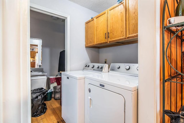 laundry room with washing machine and clothes dryer, cabinet space, a textured ceiling, and hardwood / wood-style flooring