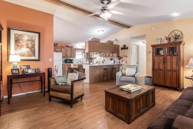 living area with lofted ceiling with beams, a ceiling fan, light wood-type flooring, and a textured ceiling